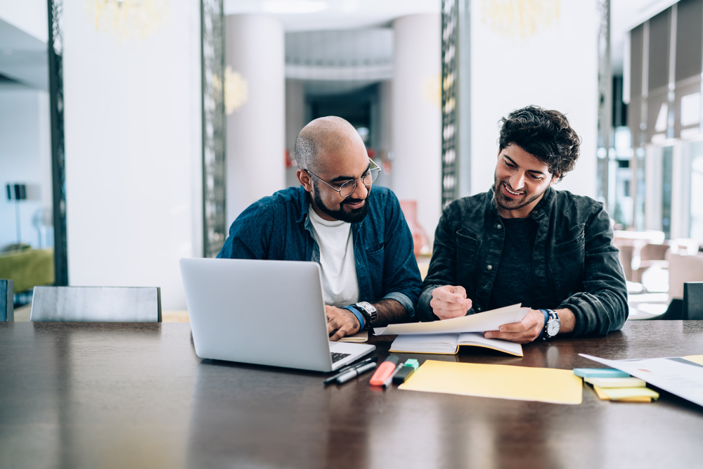 Two,Successful,Entrepreneurs,Collaborating,On,Report,Analyzing,Sitting,At,Table